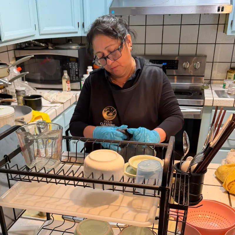Peninsula Gold Cleaning team member in uniform and gloves washing dishes in a client's kitchen